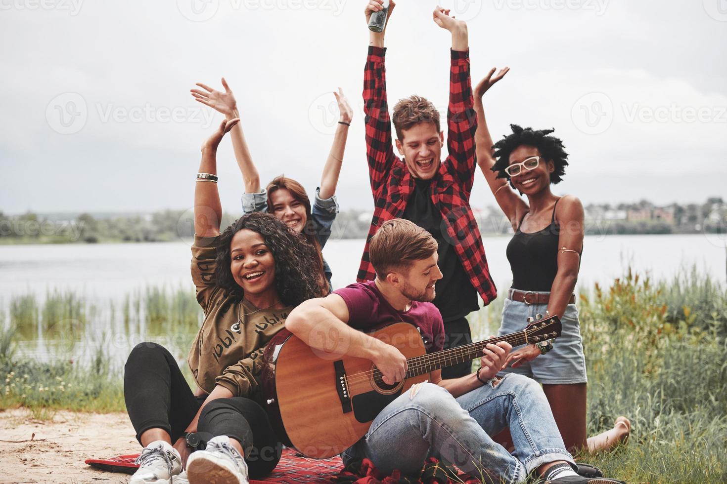 Put your hands up. Group of people have picnic on the beach. Friends have fun at weekend time photo