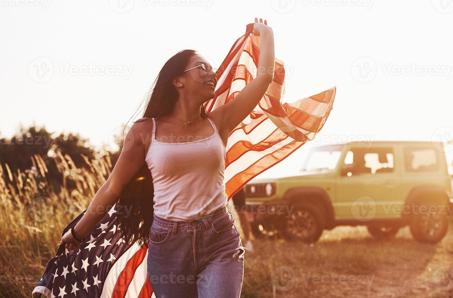 Girl runs forward. Friends have nice weekend outdoors near theirs green car with USA flag photo