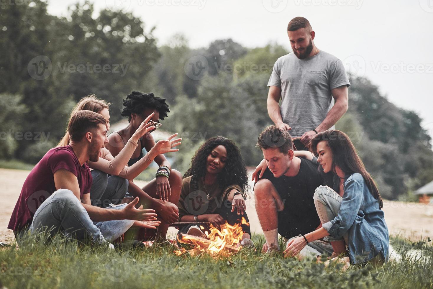 el hombre habla con interés. grupo de personas hacen picnic en la playa. los amigos se divierten el fin de semana foto