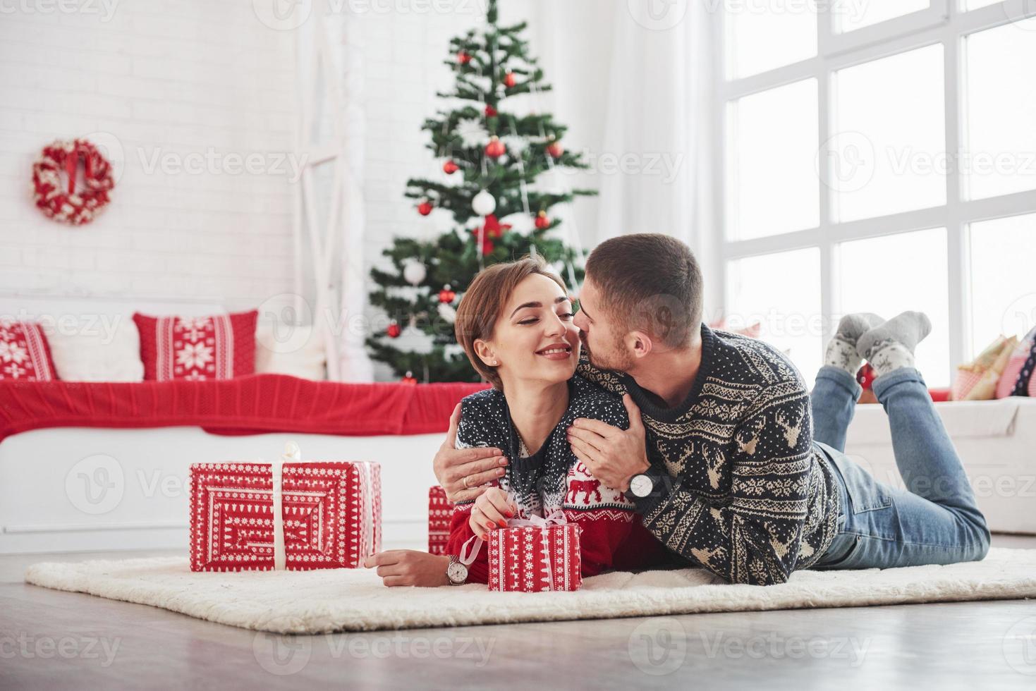 Conception of new year. Lovely young couple lying on the living room with green holiday tree at background photo