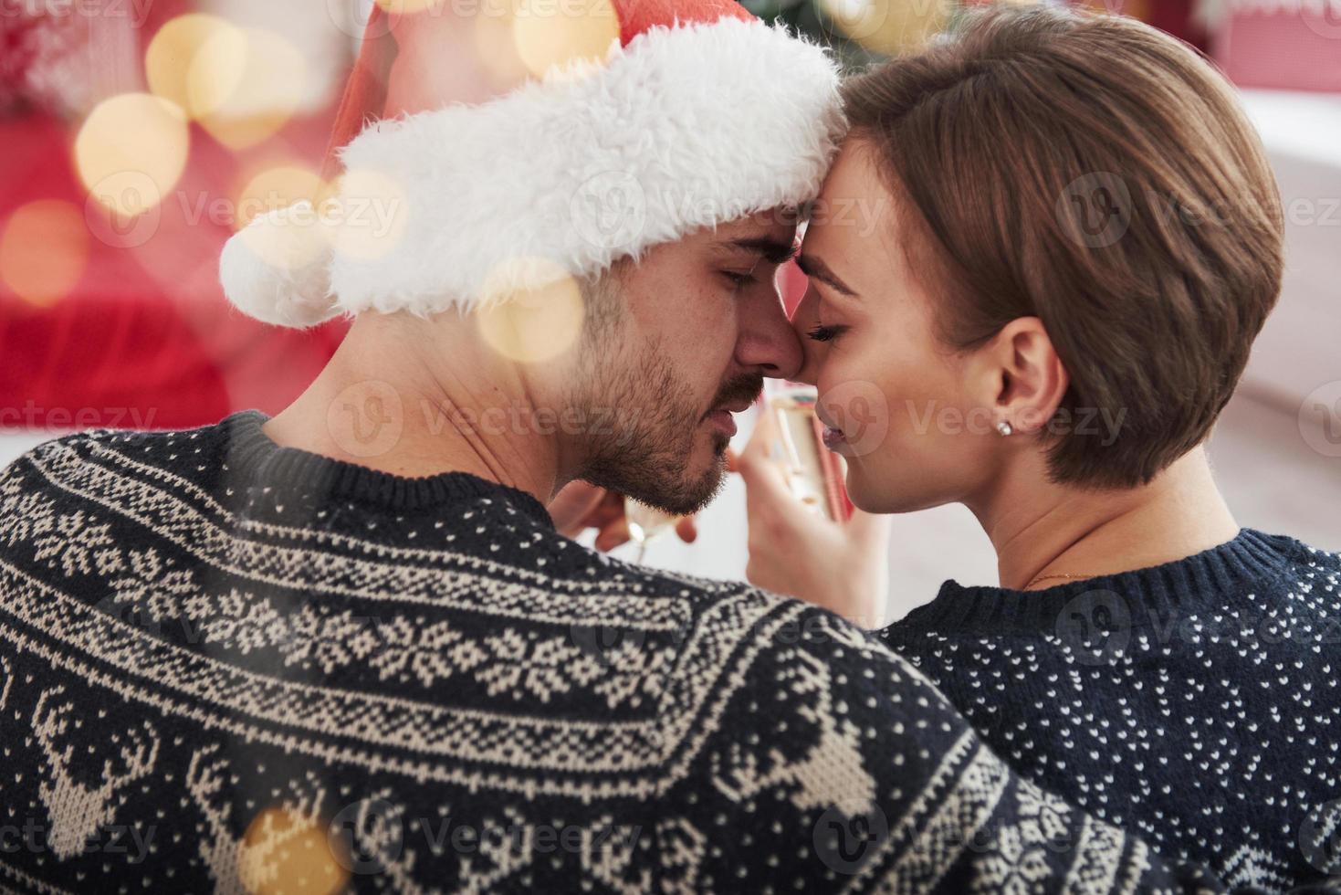 Warmth and emotions. Celebrating new year. Knocking glasses. Beautiful couple in holiday clothes sits and hugs each other. Photo from the back