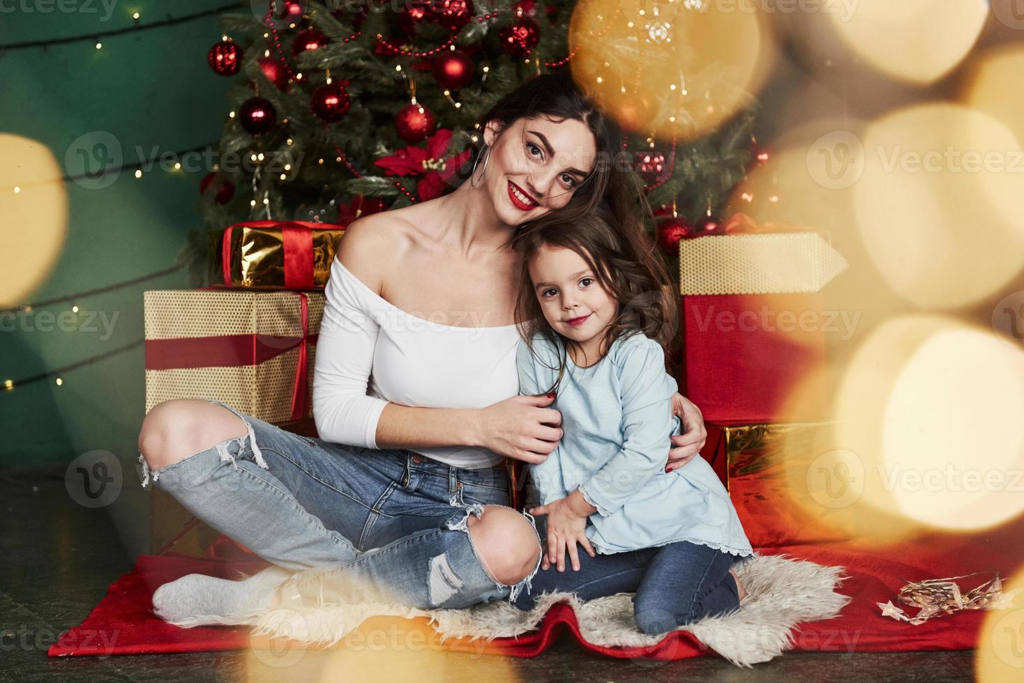 Hijo da un regalo de Navidad para mamá. Mamá agradablemente sorprendido y  lindo mira al niño. Aislado en un árbol de Año Nuevo fondo con regalos, un  fireplac Fotografía de stock 