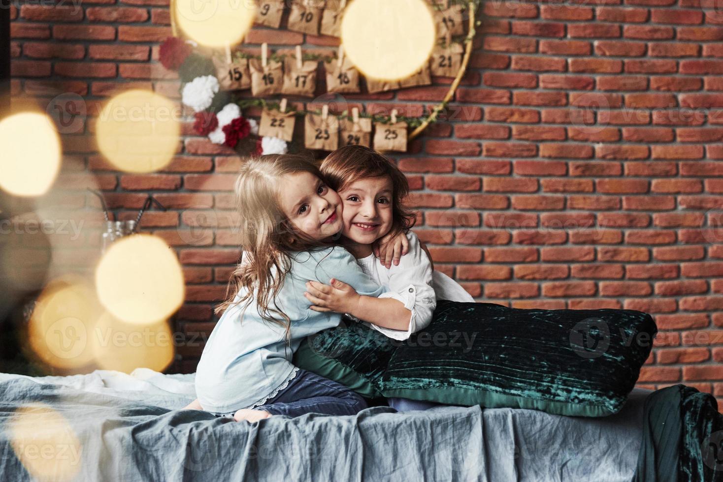 Friendly hugs. Little girls having fun on the bed with holiday interior at the background photo