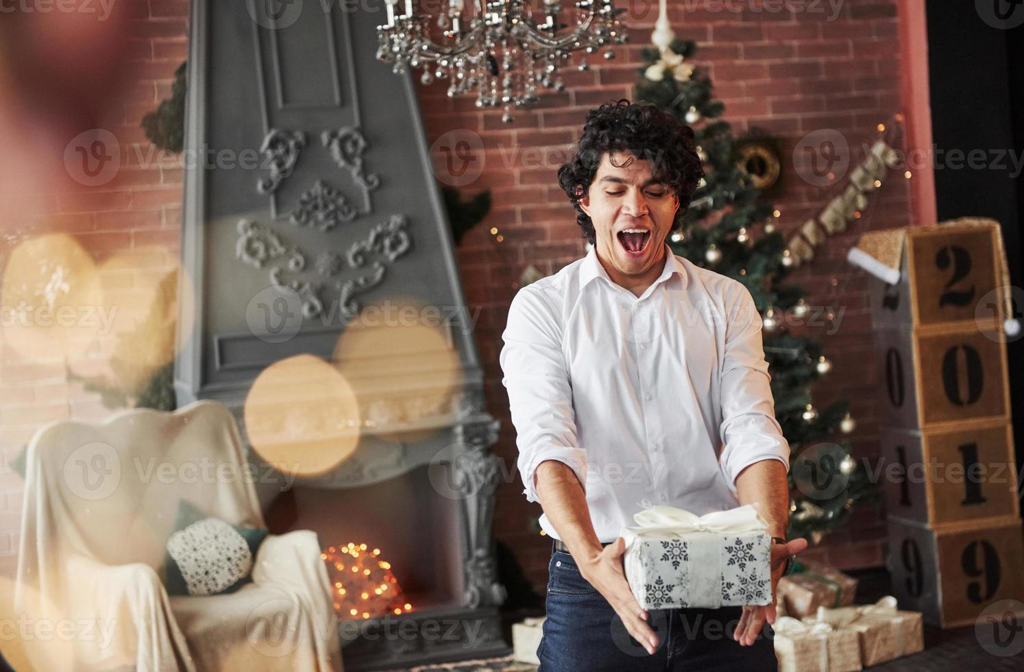Gifts time. Young man standing in the beautiful decorated room and holding white box with present in the New year time photo