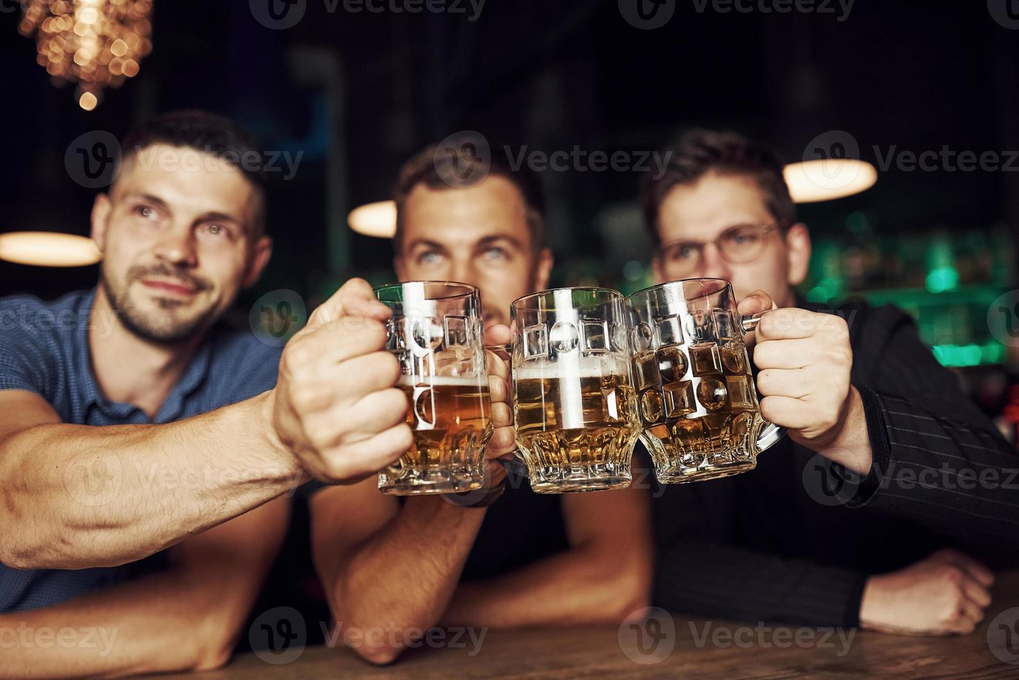 golpeando vasos. tres aficionados al deporte en un bar viendo fútbol. con cerveza en las manos foto