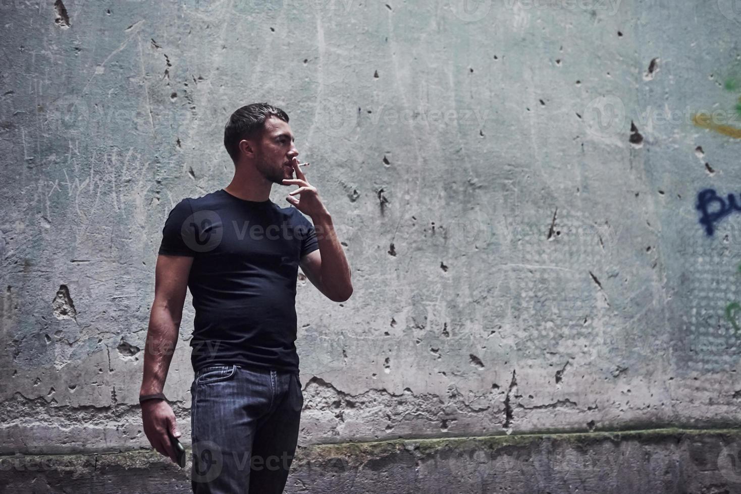 Portrait of man in black shirt smoking on the background of old cracked wall photo