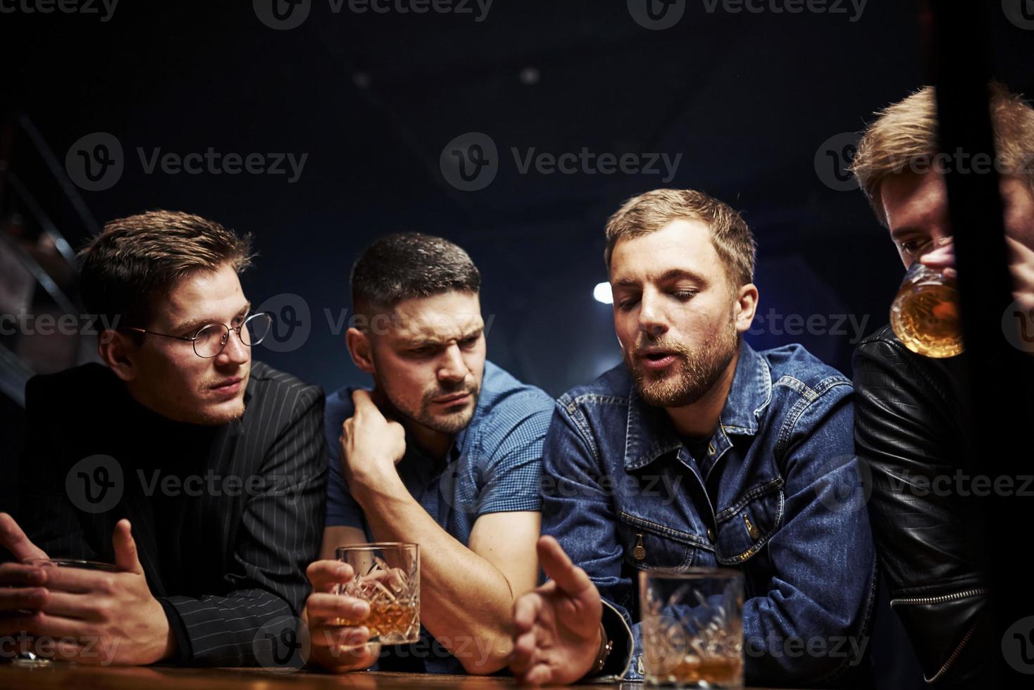 Front view. Friends resting in the pub with alcohol in hands. Having conversation photo