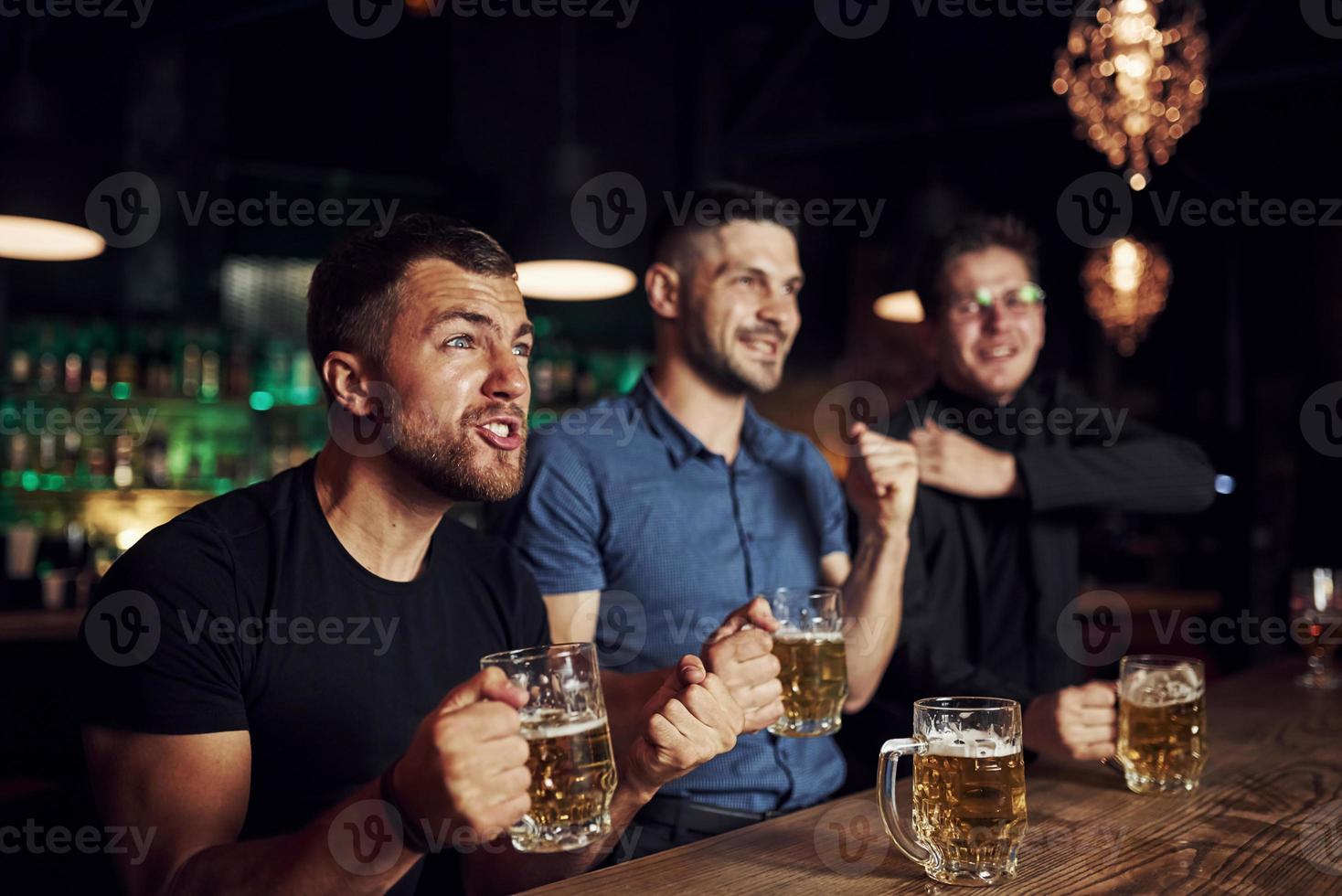 Three sports fans in a bar watching soccer. With beer in hands photo