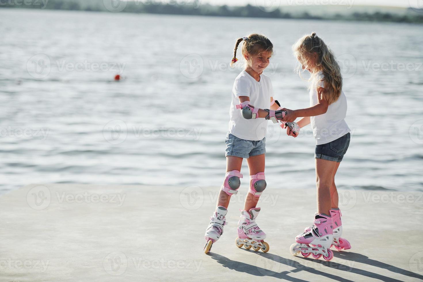 Two kids learning how to ride on roller skates at daytime near the lake