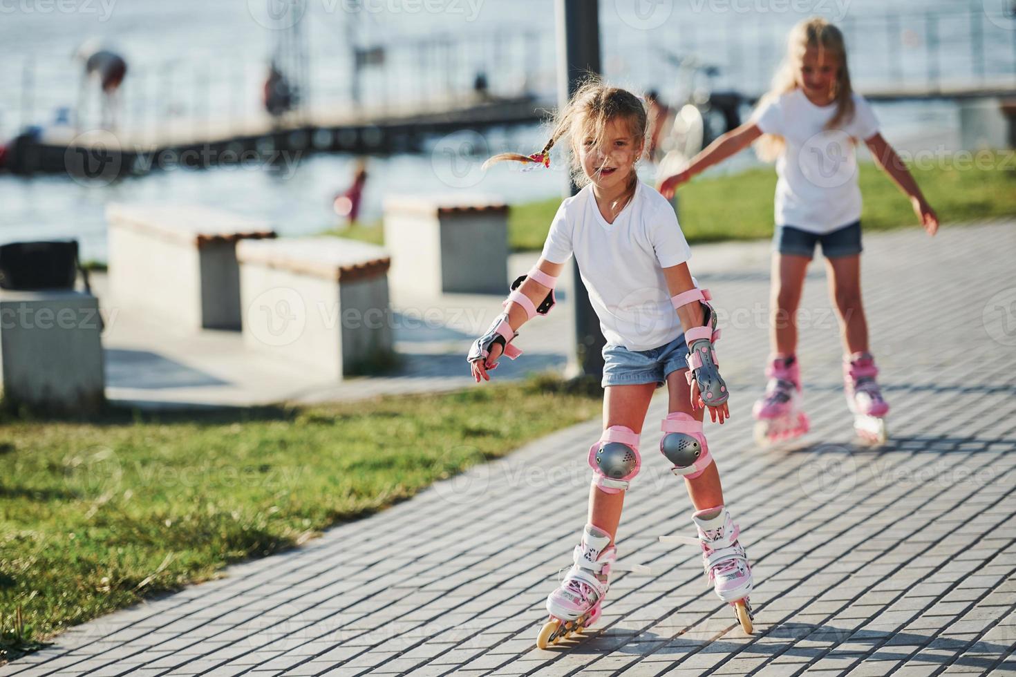 Two cute kids riding by roller skates in the park at daytime photo