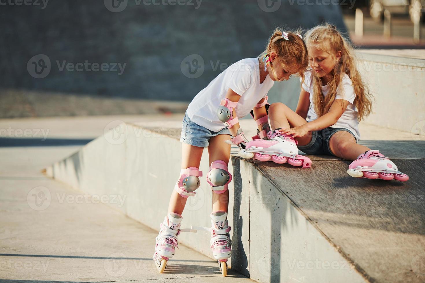 Warm weather. On the ramp for extreme sports. Two little girls with roller skates outdoors have fun photo