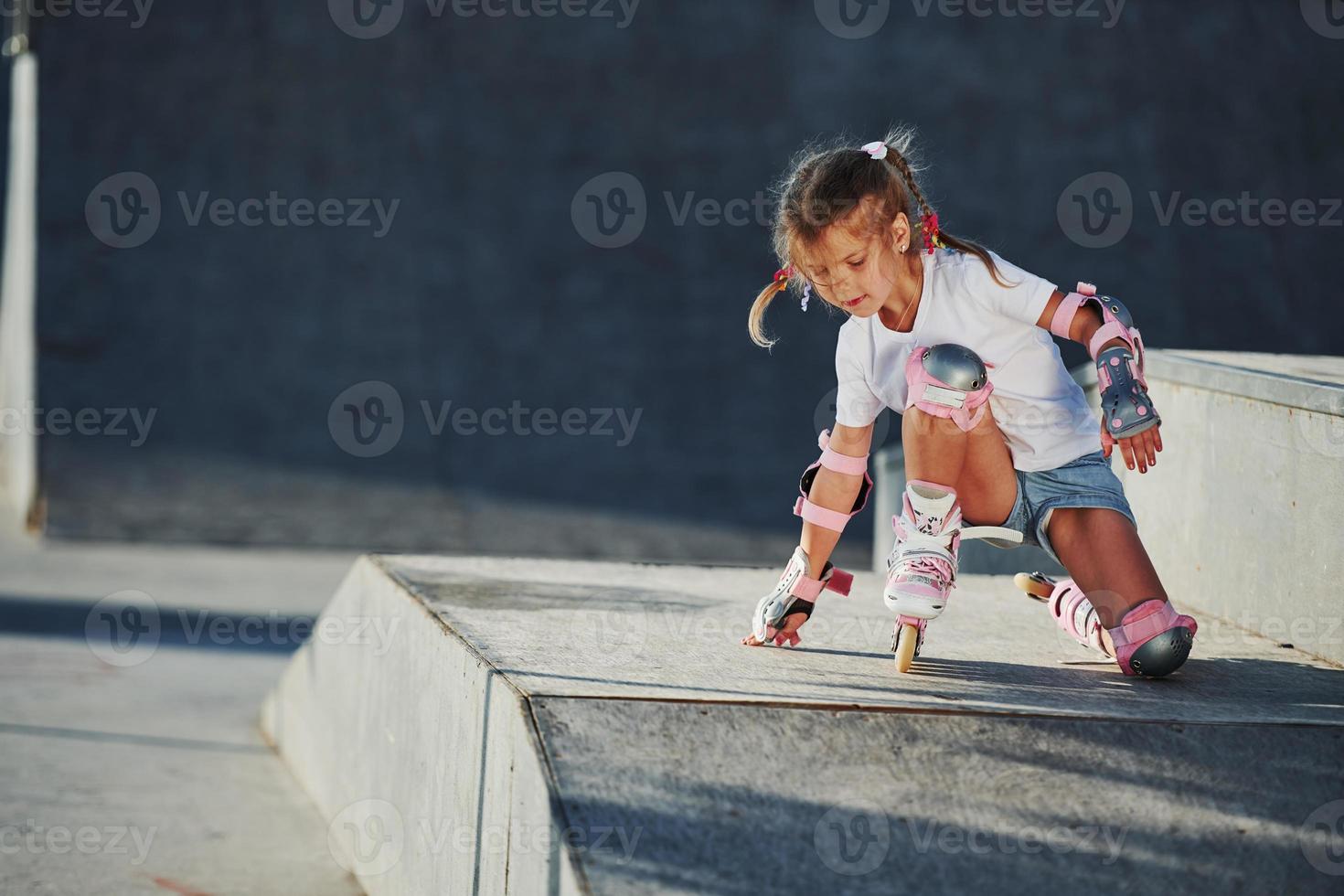 Cute little girl with roller skates outdoors sits on the ramp for extreme sports photo