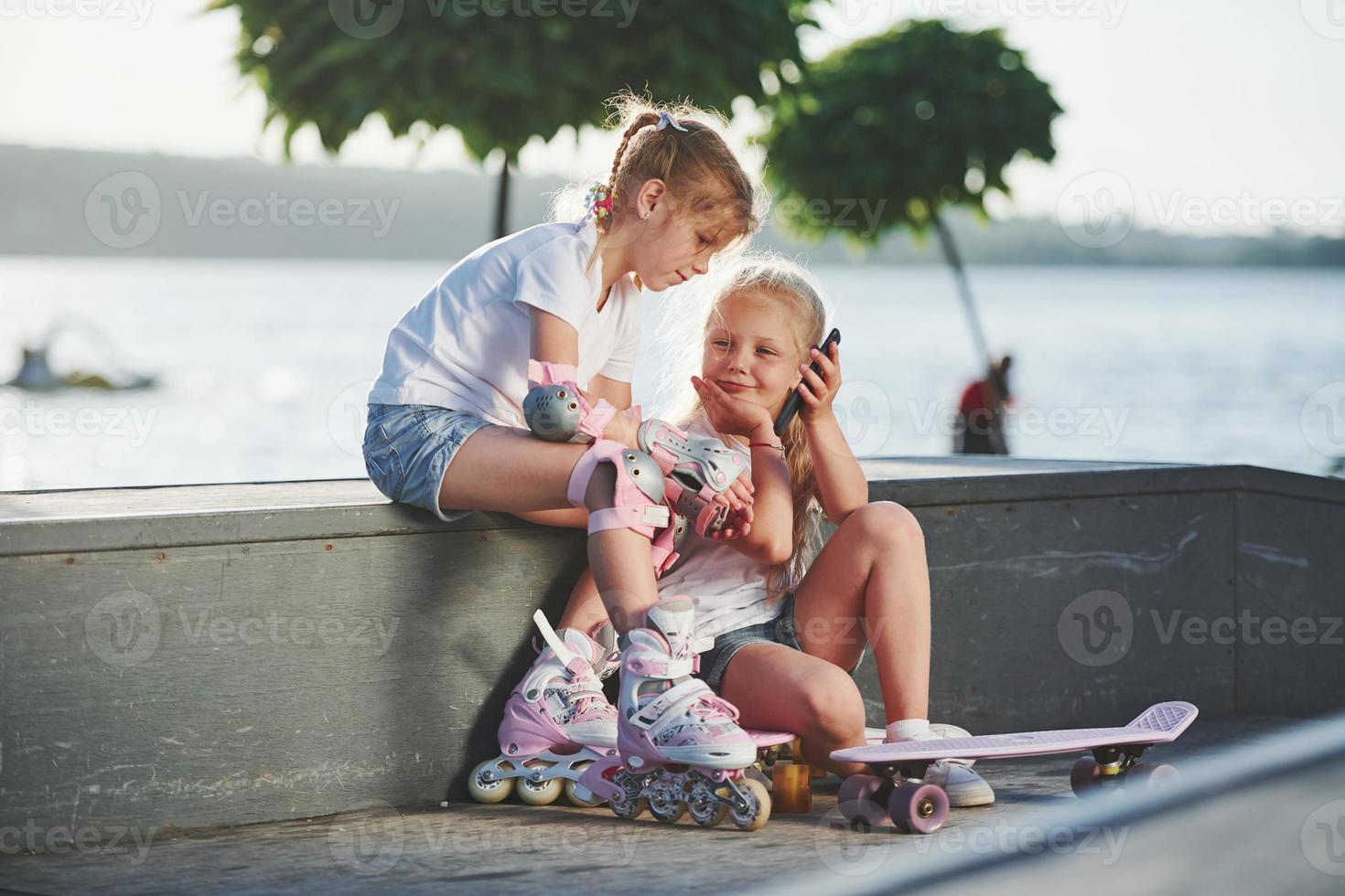 Talking with each other. On the ramp for extreme sports. Two little girls with roller skates outdoors have fun photo