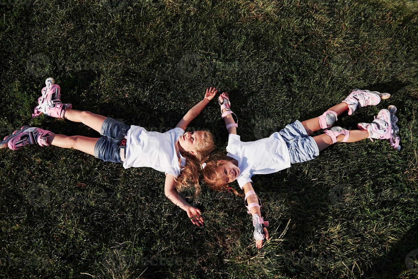 Top view. Feeling freedom. Two female kids lying on the green grass at summertime photo