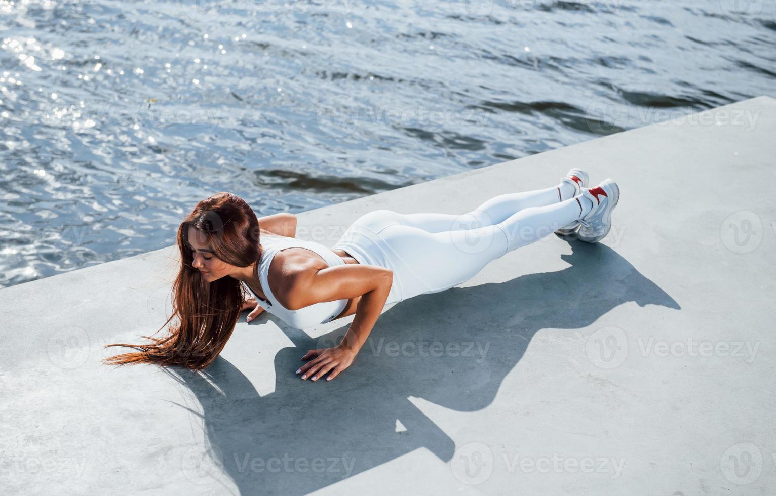 Doing push ups. Shot of sportive woman doing fitness exercises near the lake at daytime photo