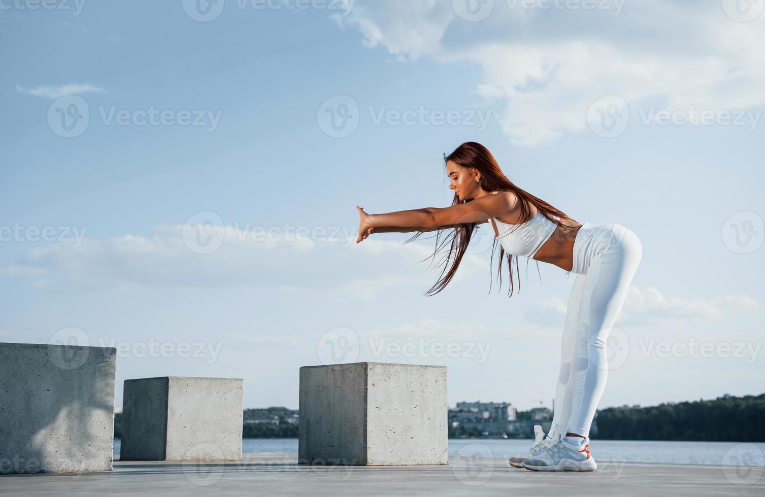 Shot of sportive woman doing fitness exercises near the lake at daytime photo