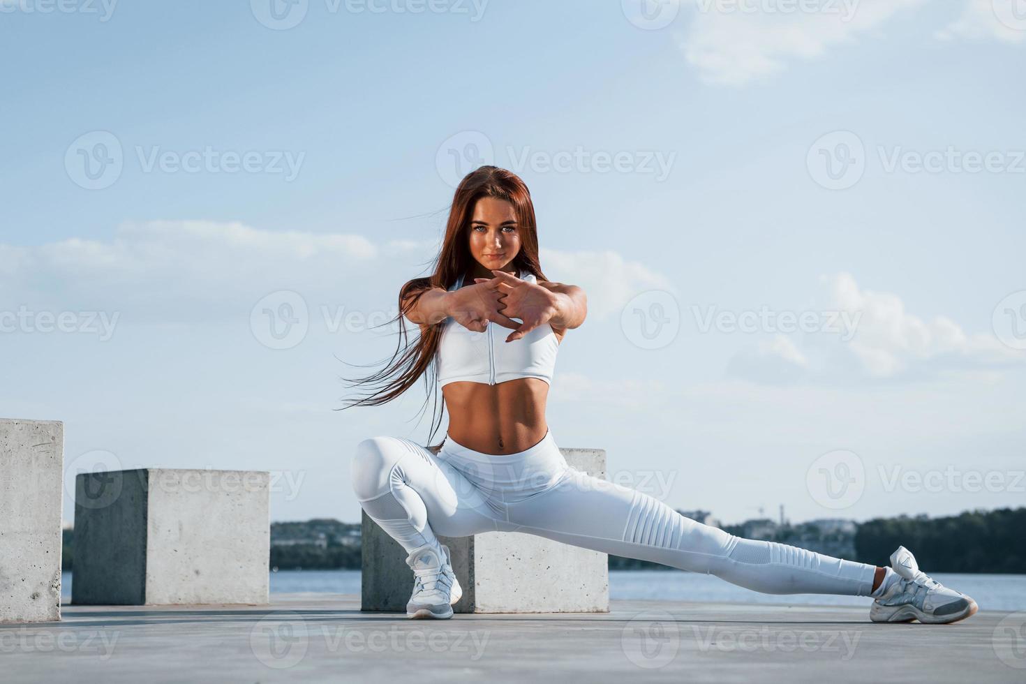 Exercises for legs. Shot of sportive woman doing fitness near the lake at daytime photo