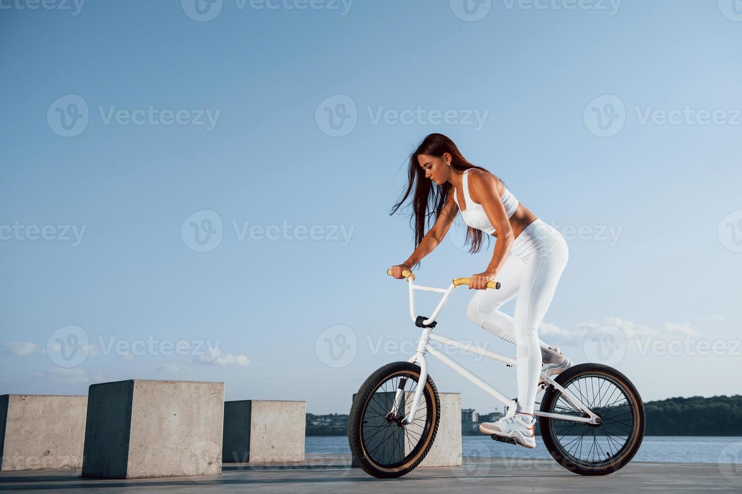 Female rider is on the bike at daytime near the lake. Fitness woman in sportive clothes photo