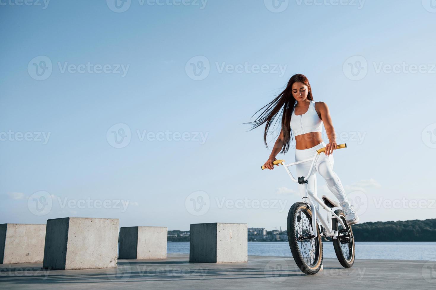 Female rider is on the bike at daytime near the lake. Fitness woman in sportive clothes photo