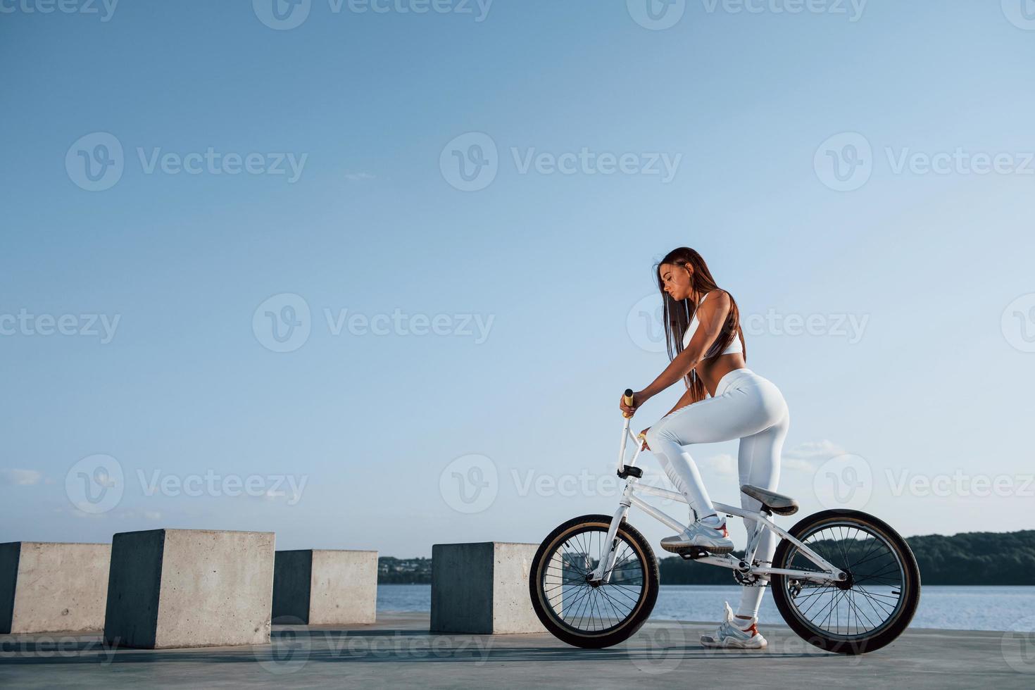 Female rider is on the bike at daytime near the lake. Fitness woman in sportive clothes photo