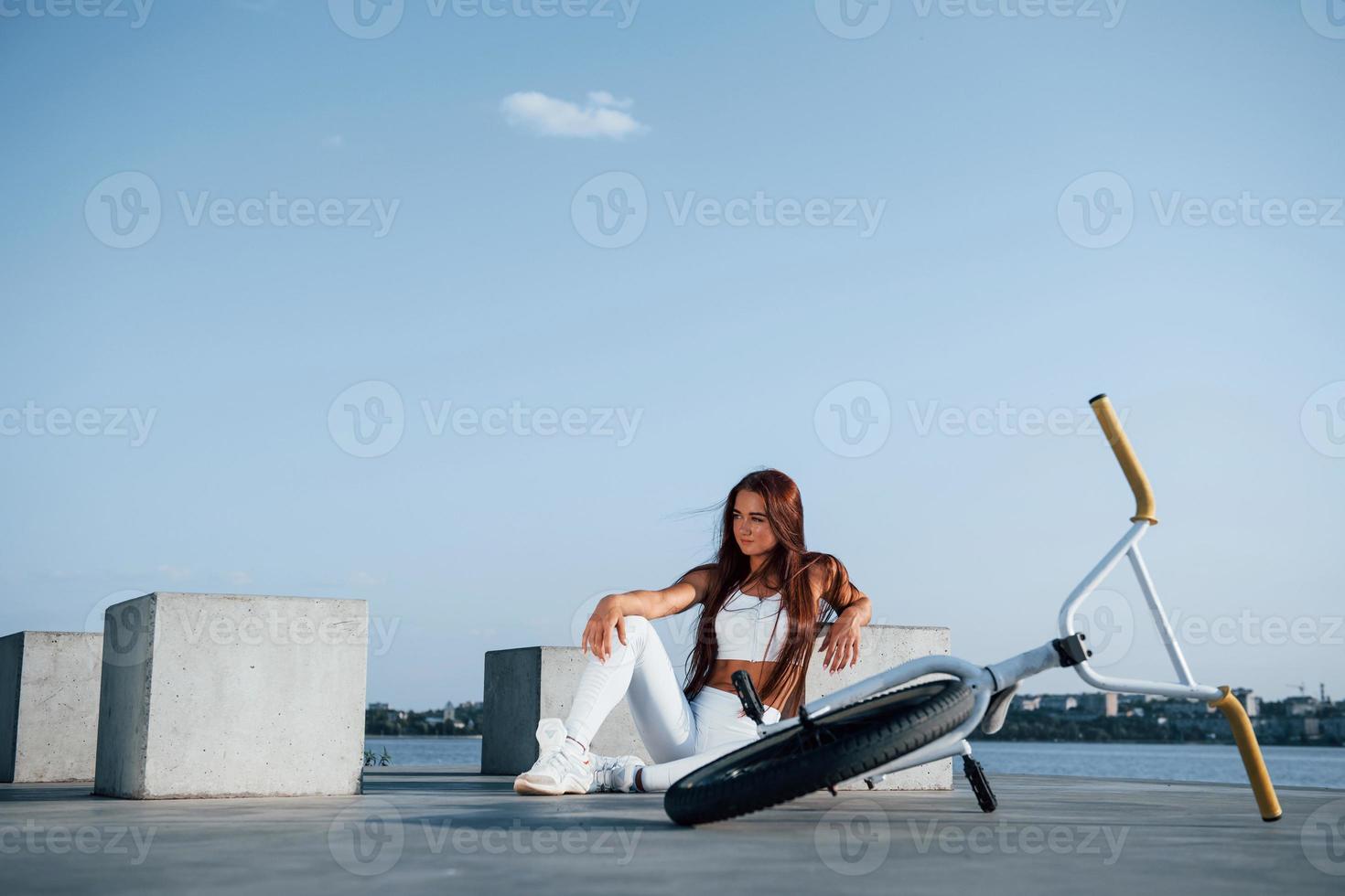 Near the bike. Fitness woman having a rest near the lake at daytime. Beautiful sunlight photo