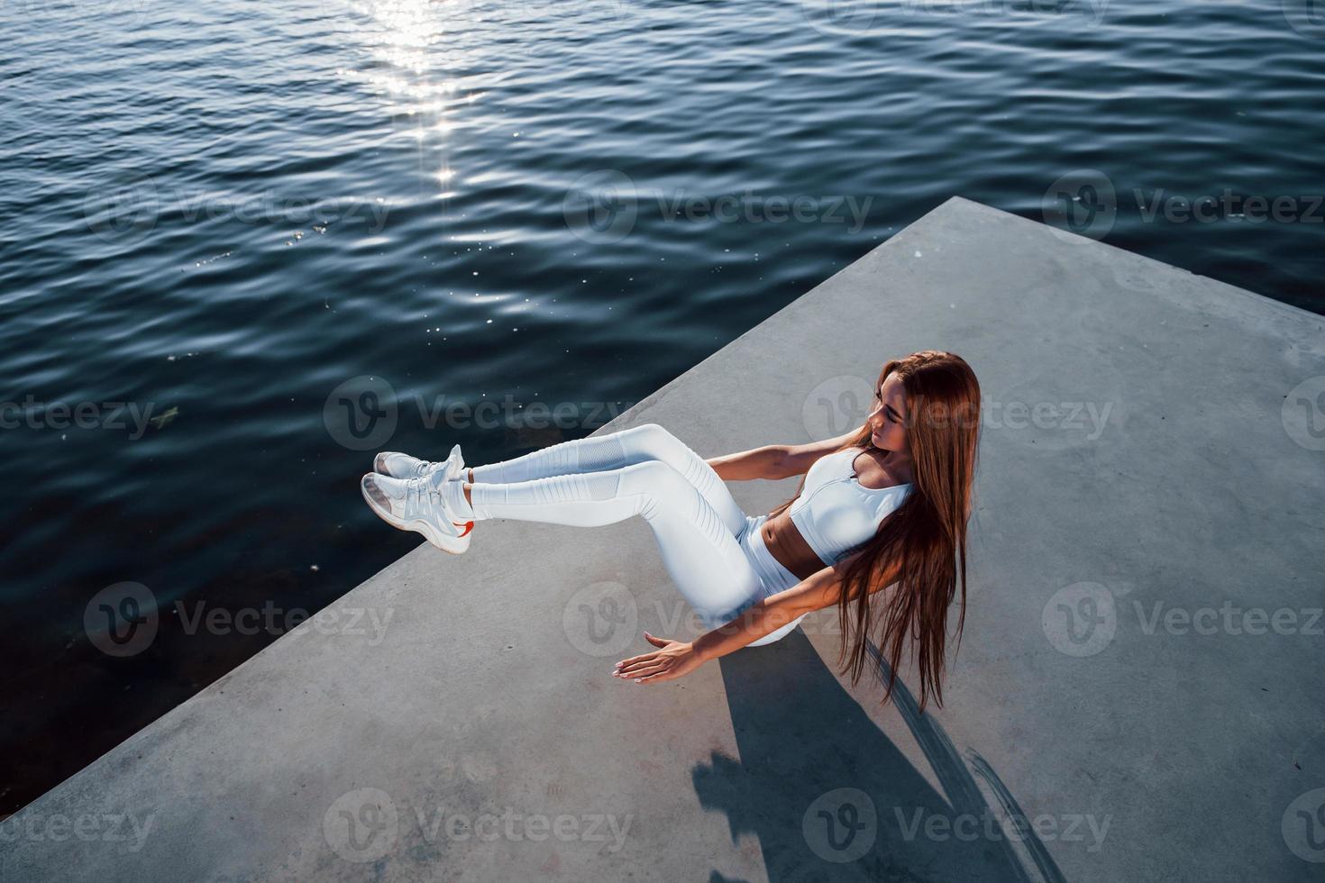 Shot of sportive woman doing fitness exercises near the lake at daytime photo