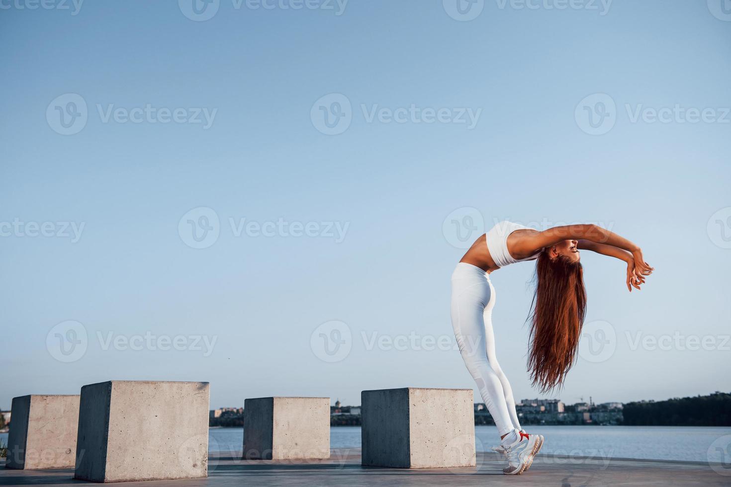 Shot of sportive woman doing fitness exercises near the lake at daytime photo