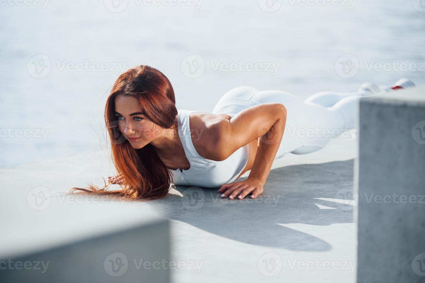 Doing push ups. Shot of sportive woman doing fitness exercises near the lake at daytime photo