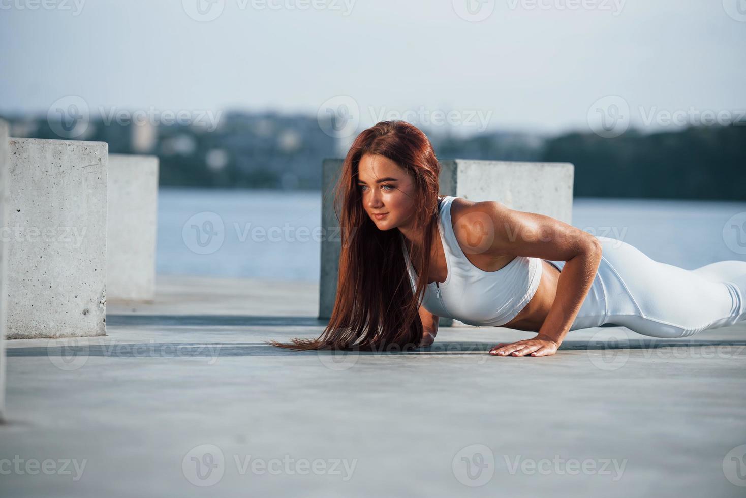 Shot of sportive woman doing fitness exercises near the lake at daytime photo