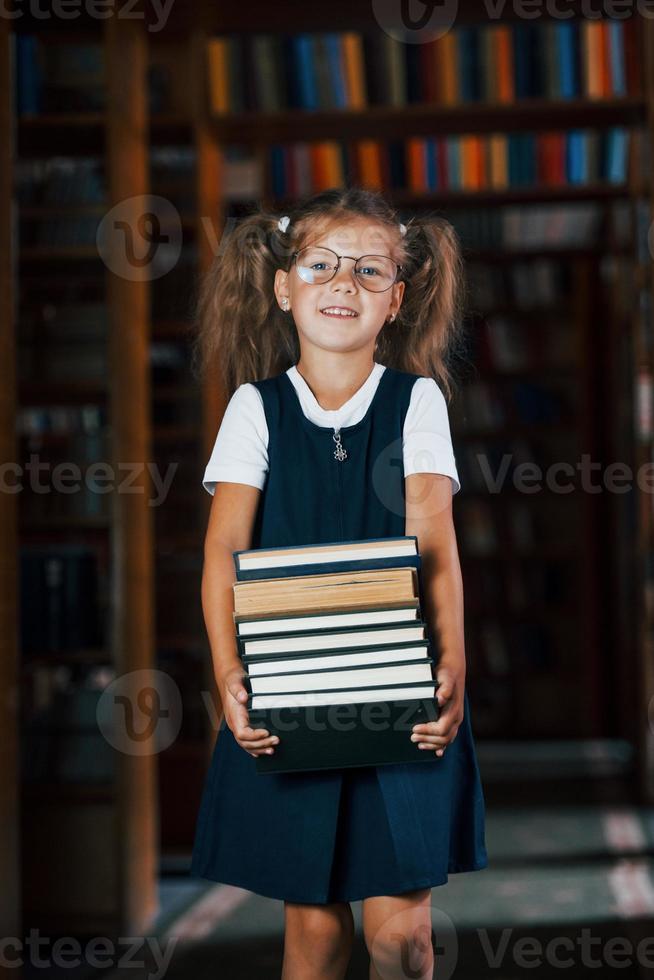 linda niñita con anteojos se encuentra en la biblioteca llena de libros. concepción de la educación foto