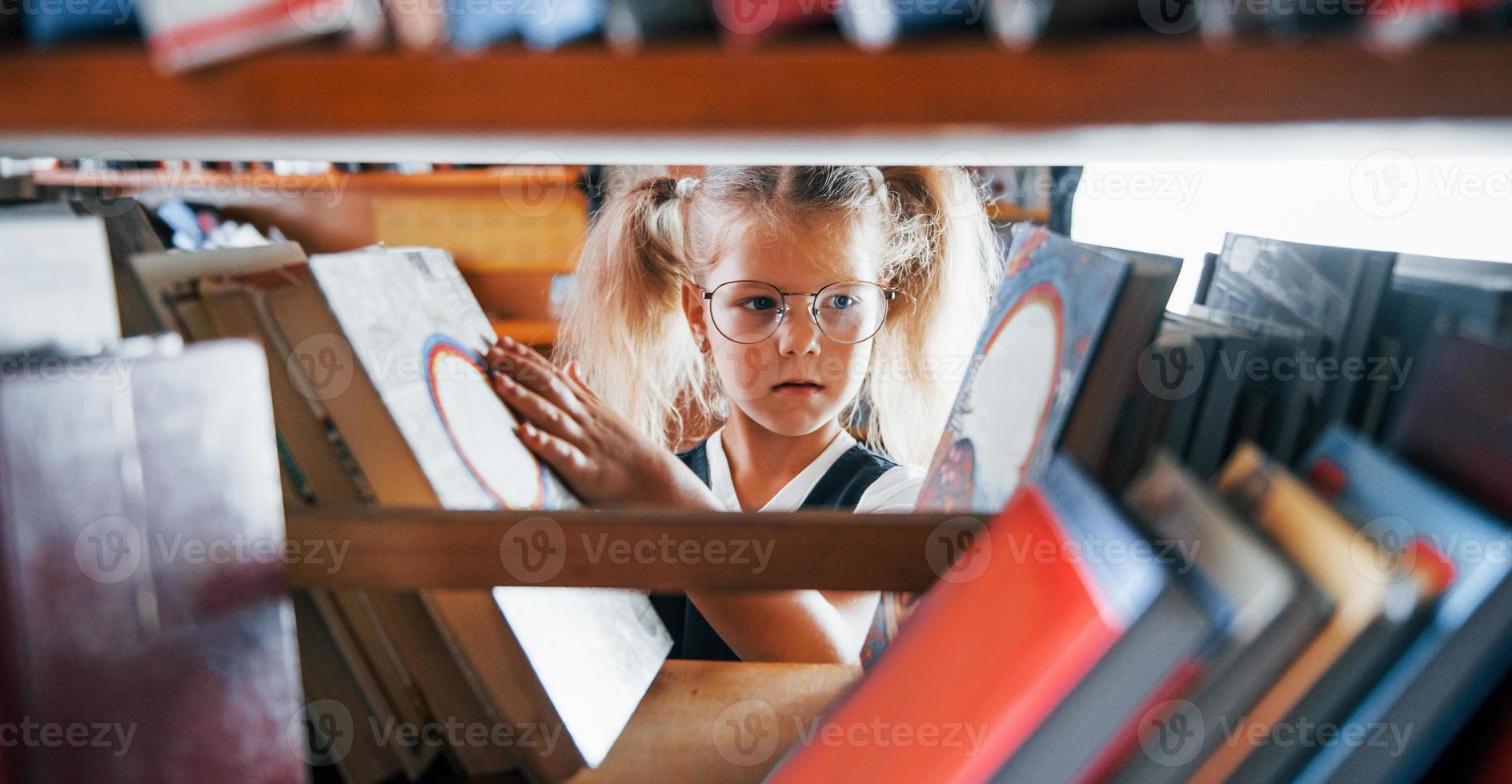niña con gafas buscando un libro en la biblioteca. concepción de la educación foto