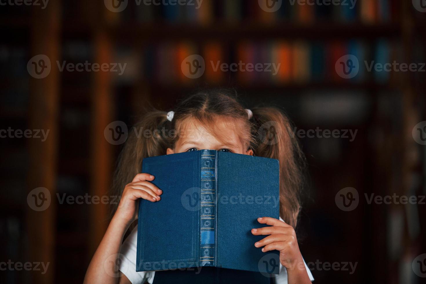 Having fun. Cute little girl stands in the library full of books. Conception of education photo