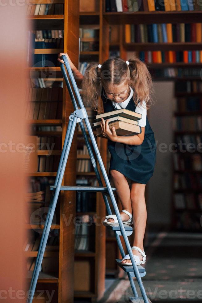 School girl on the ladder in library full of books. Education conception photo