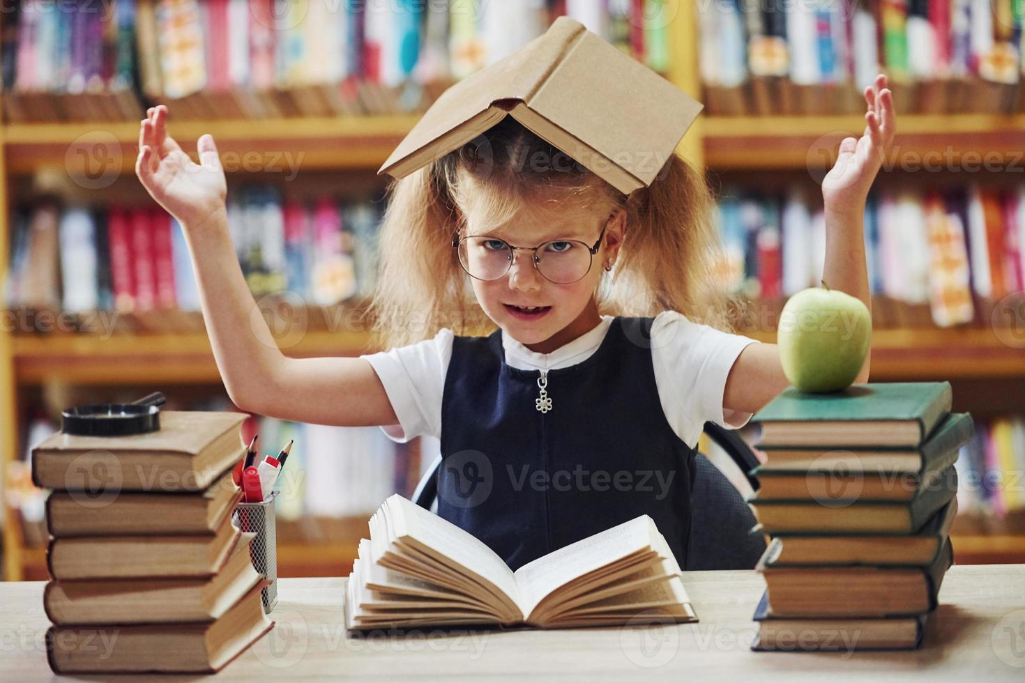 estado de ánimo juguetón. linda niña con coletas está en la biblioteca. manzana en los libros foto