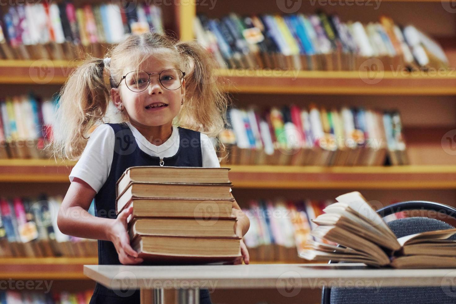 Holding books. Cute little girl with pigtails is in the library photo