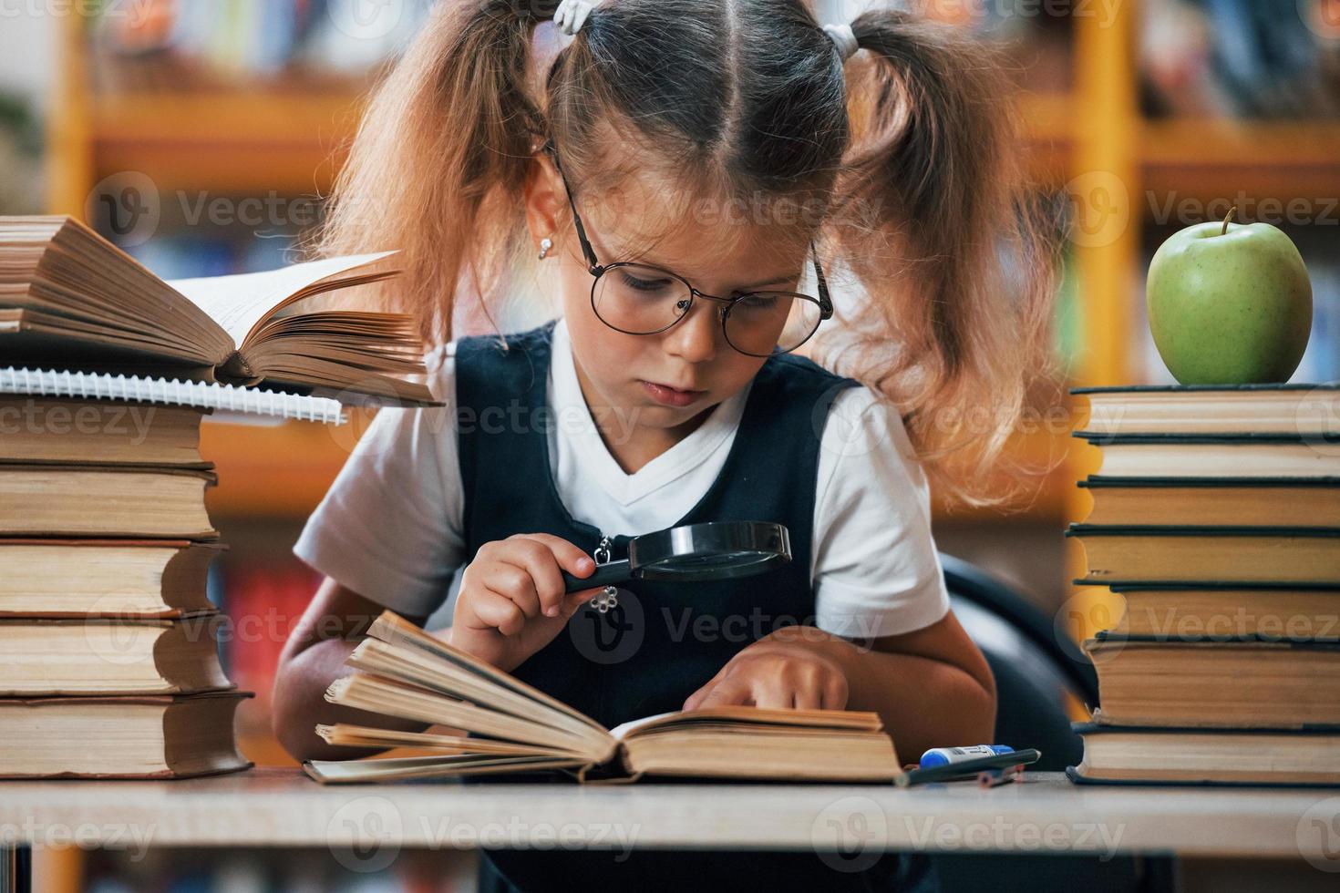 vista frontal. linda niña con coletas está en la biblioteca. manzana en los libros foto