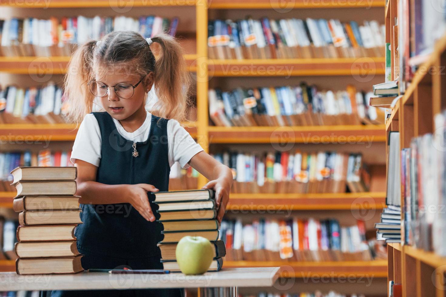 Cute little girl with pigtails is in the library. Apple on the books photo
