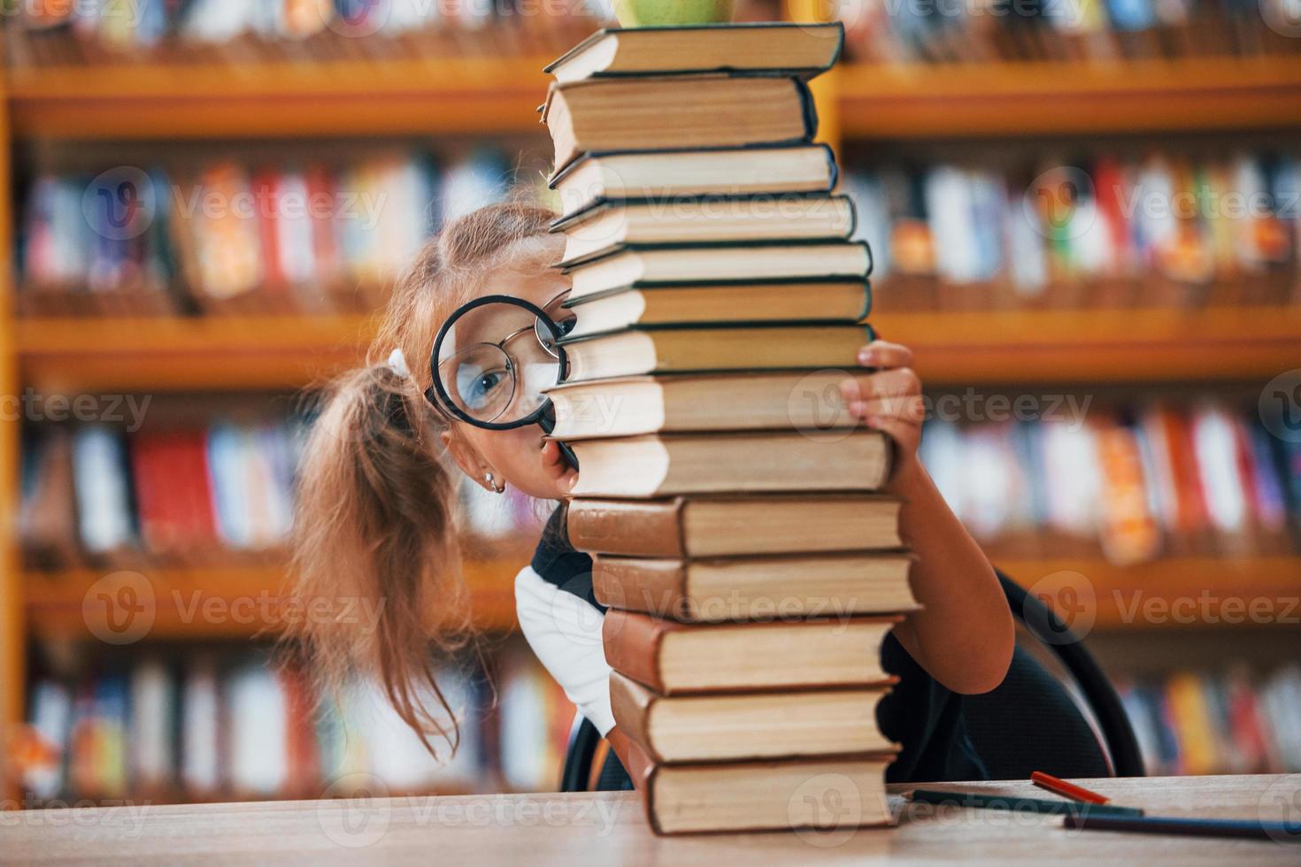 Cute little girl with pigtails is in the library. Apple on the books photo