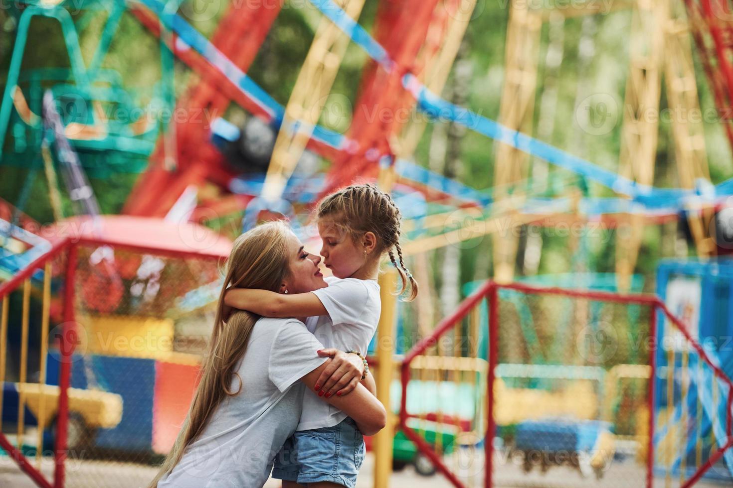 Embracing each other. Cheerful little girl her mother have a good time in the park together near attractions photo