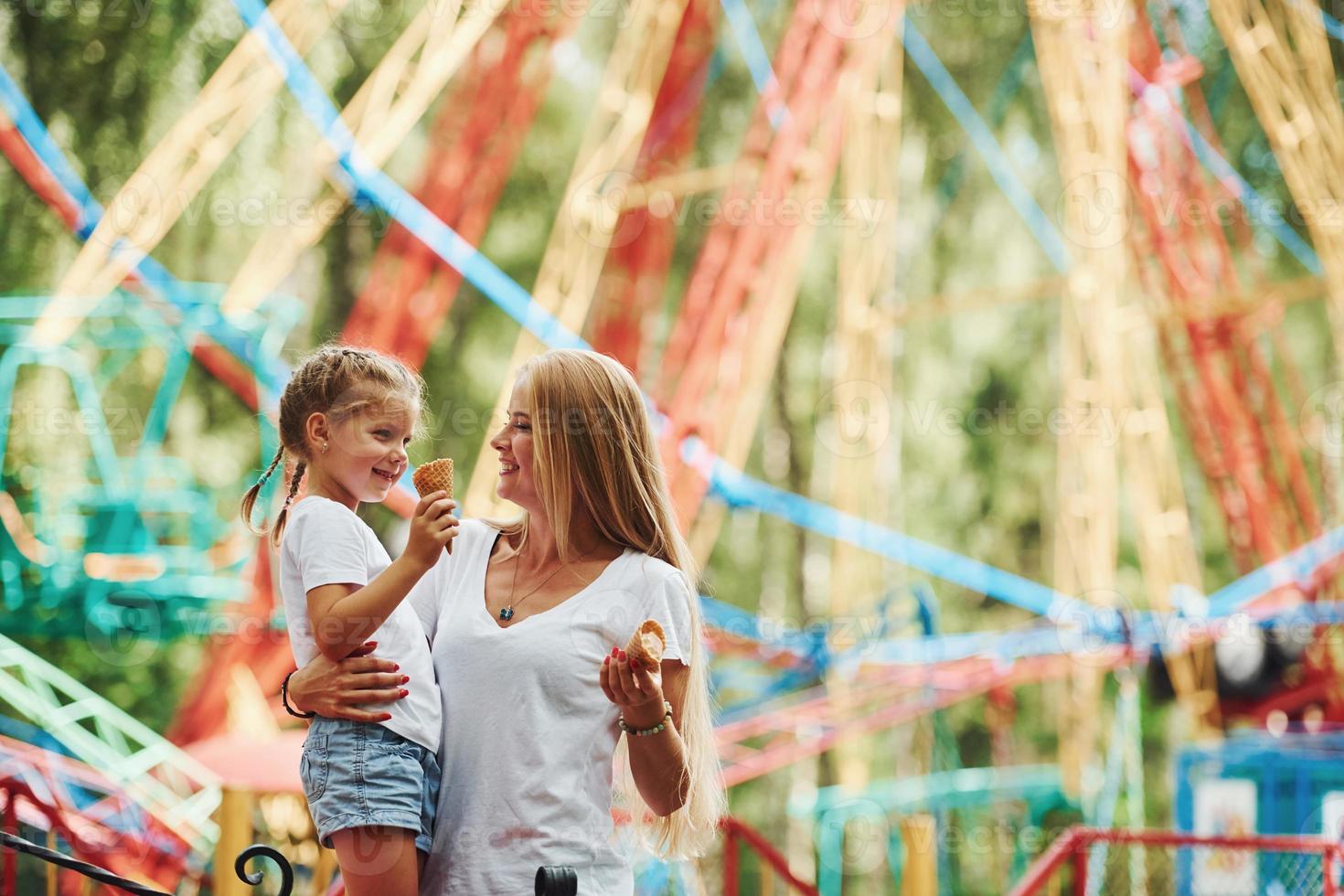 Comiendo helado. niña alegre su madre se divierten juntos en el parque cerca de las atracciones foto