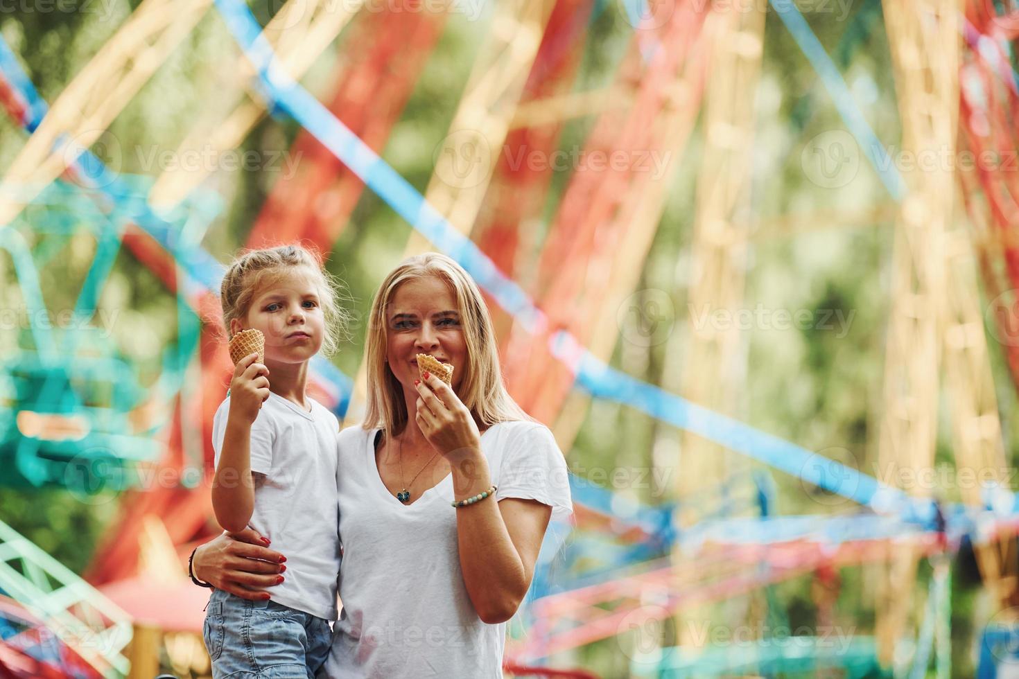 Eating ice cream. Cheerful little girl her mother have a good time in the park together near attractions photo