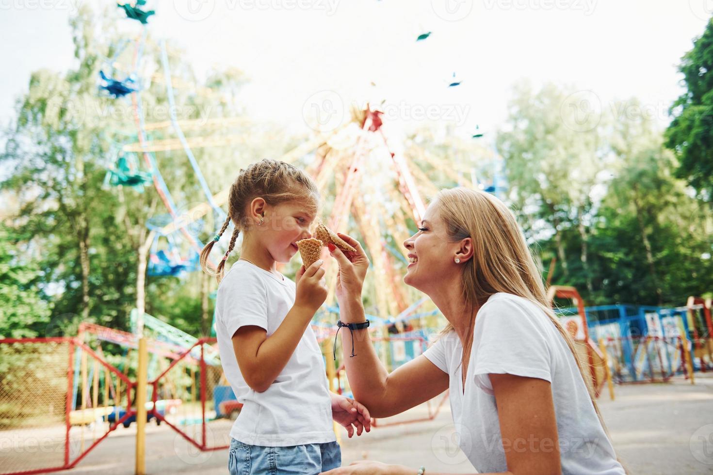 Eating ice cream. Cheerful little girl her mother have a good time in the park together near attractions photo