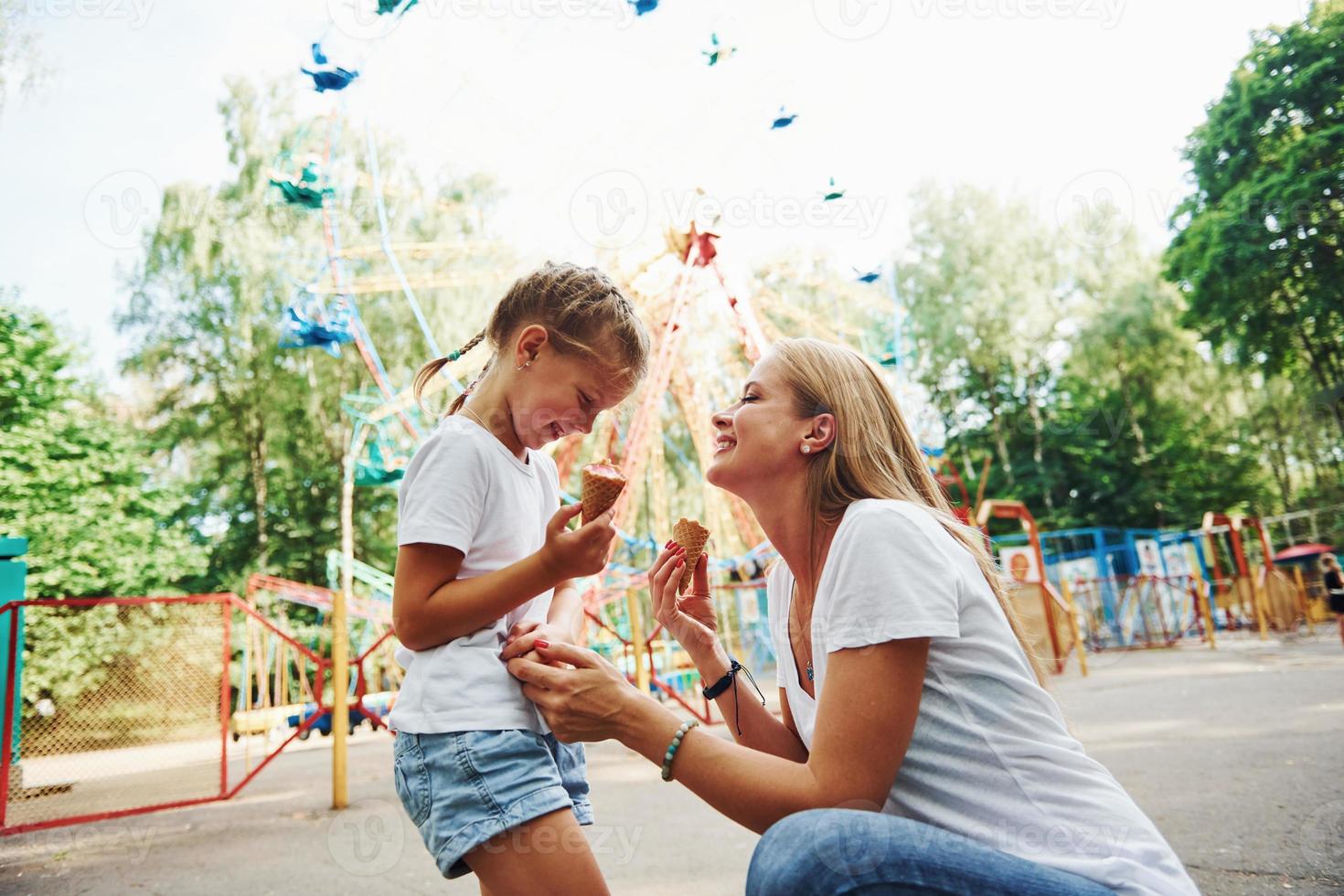 Eating ice cream. Cheerful little girl her mother have a good time in the park together near attractions photo