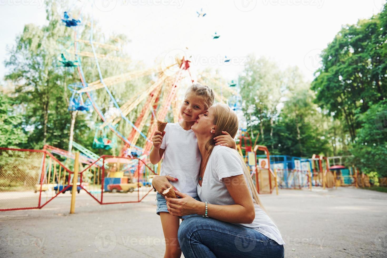 Comiendo helado. niña alegre su madre se divierten juntos en el parque cerca de las atracciones foto