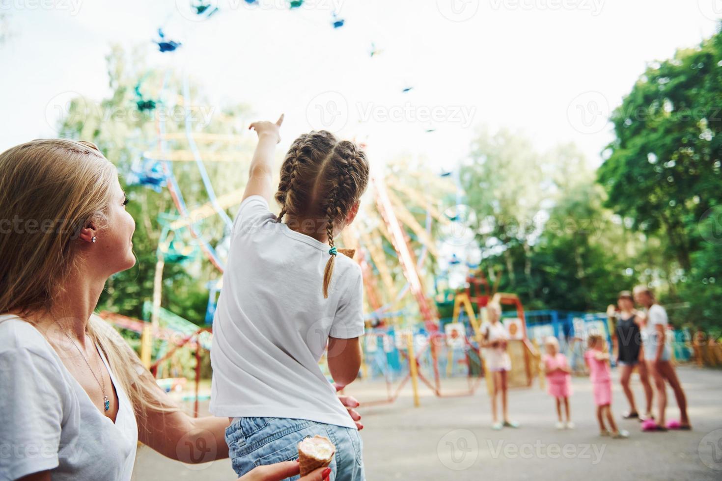 Eating ice cream. Cheerful little girl her mother have a good time in the park together near attractions photo