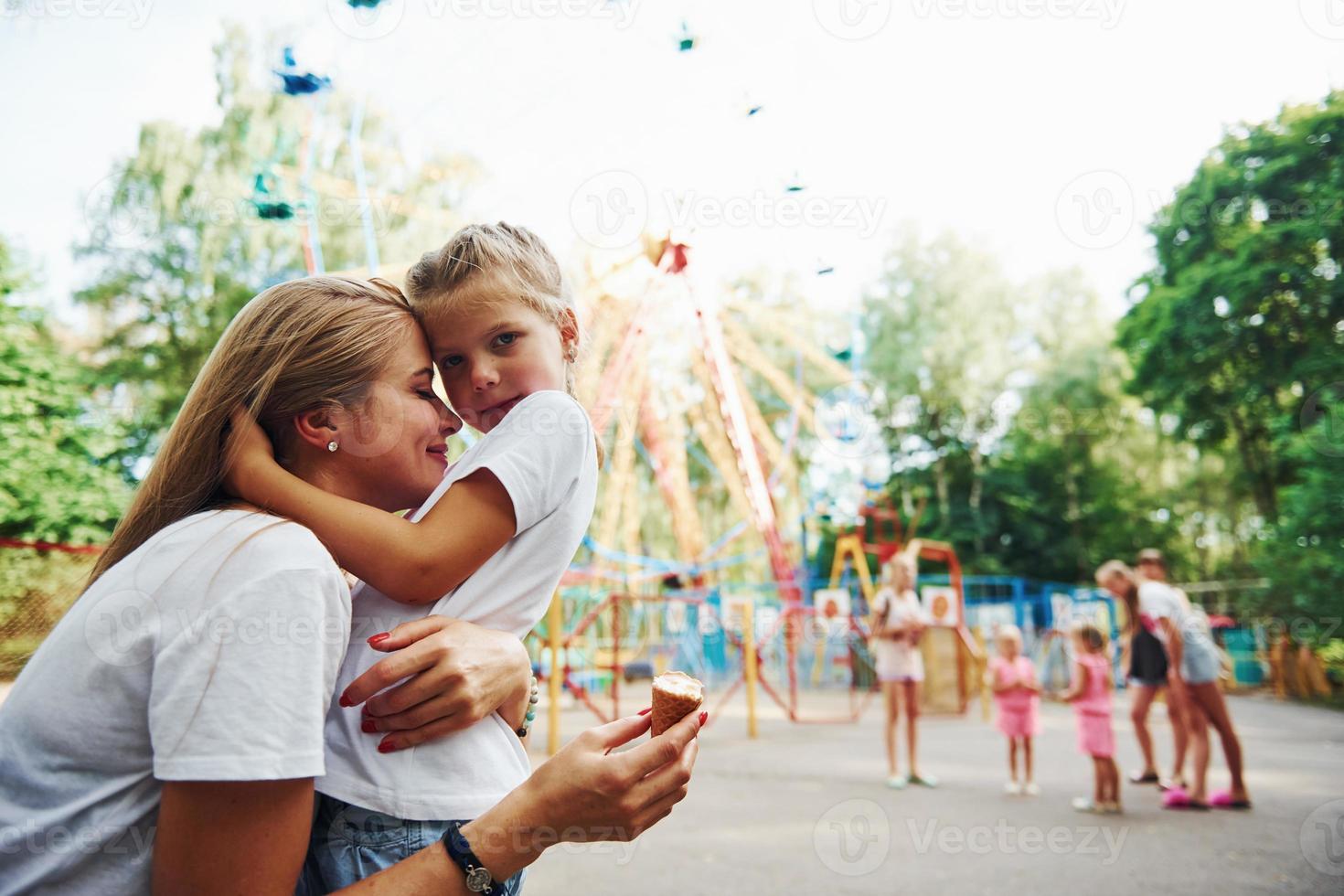 Comiendo helado. niña alegre su madre se divierten juntos en el parque cerca de las atracciones foto