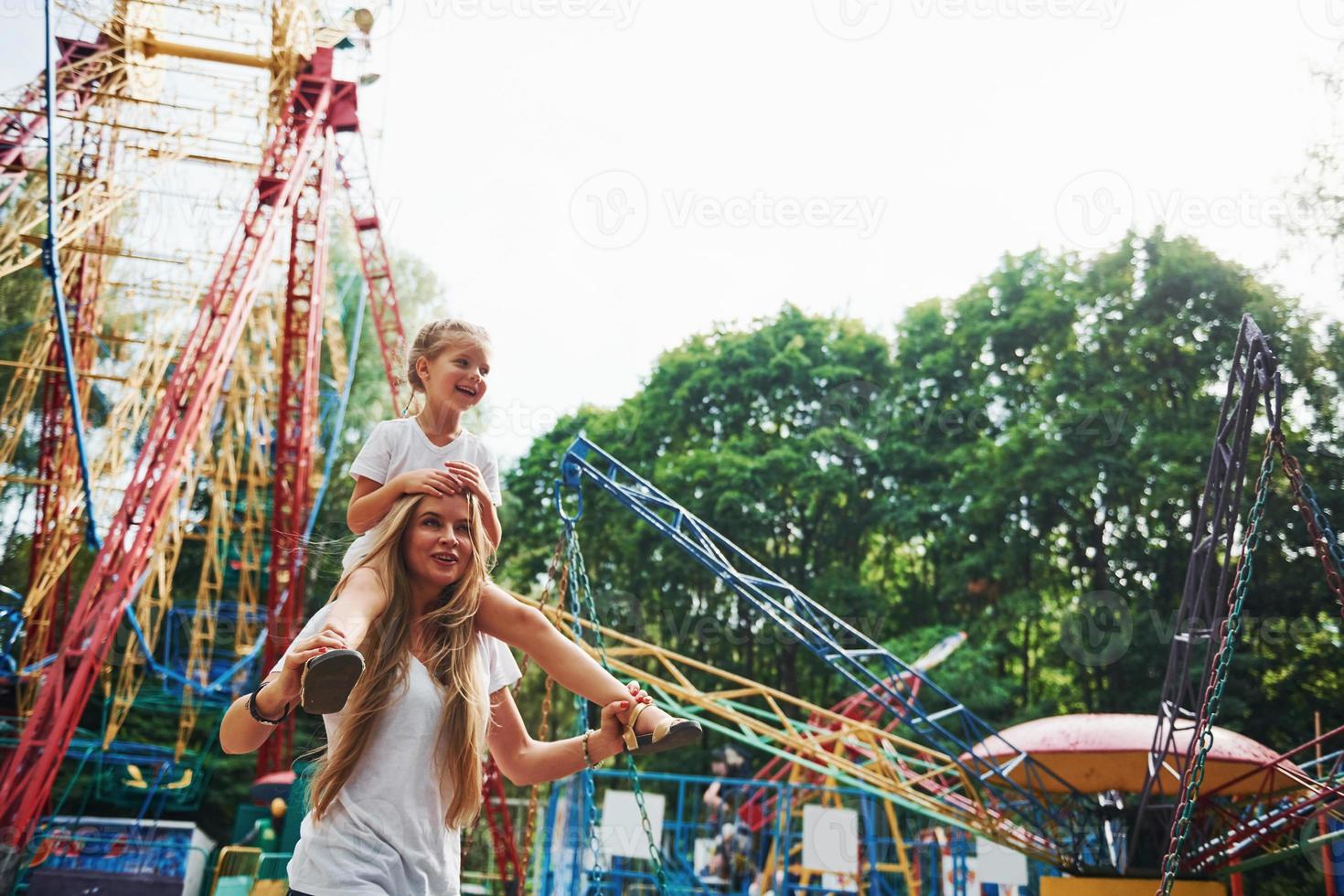 niña alegre su madre se divierten juntos en el parque cerca de las atracciones foto