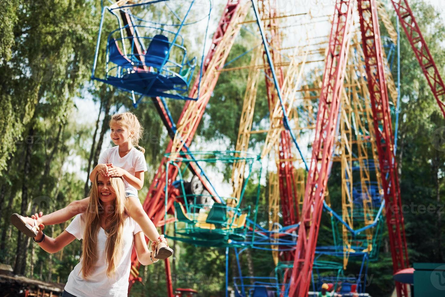 Cheerful little girl her mother have a good time in the park together near attractions photo