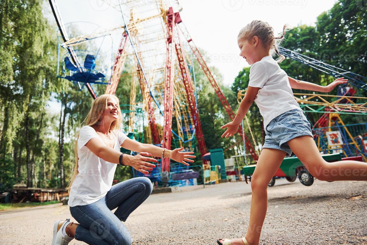 Running and playing. Cheerful little girl her mother have a good time in the park together near attractions photo