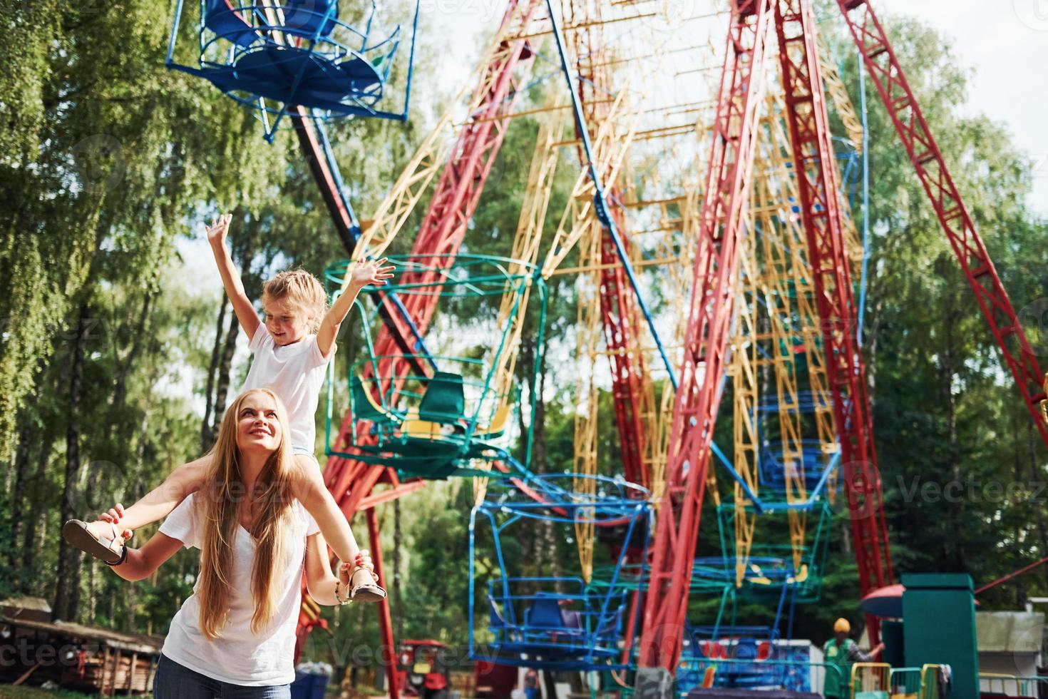 Cheerful little girl her mother have a good time in the park together near attractions photo